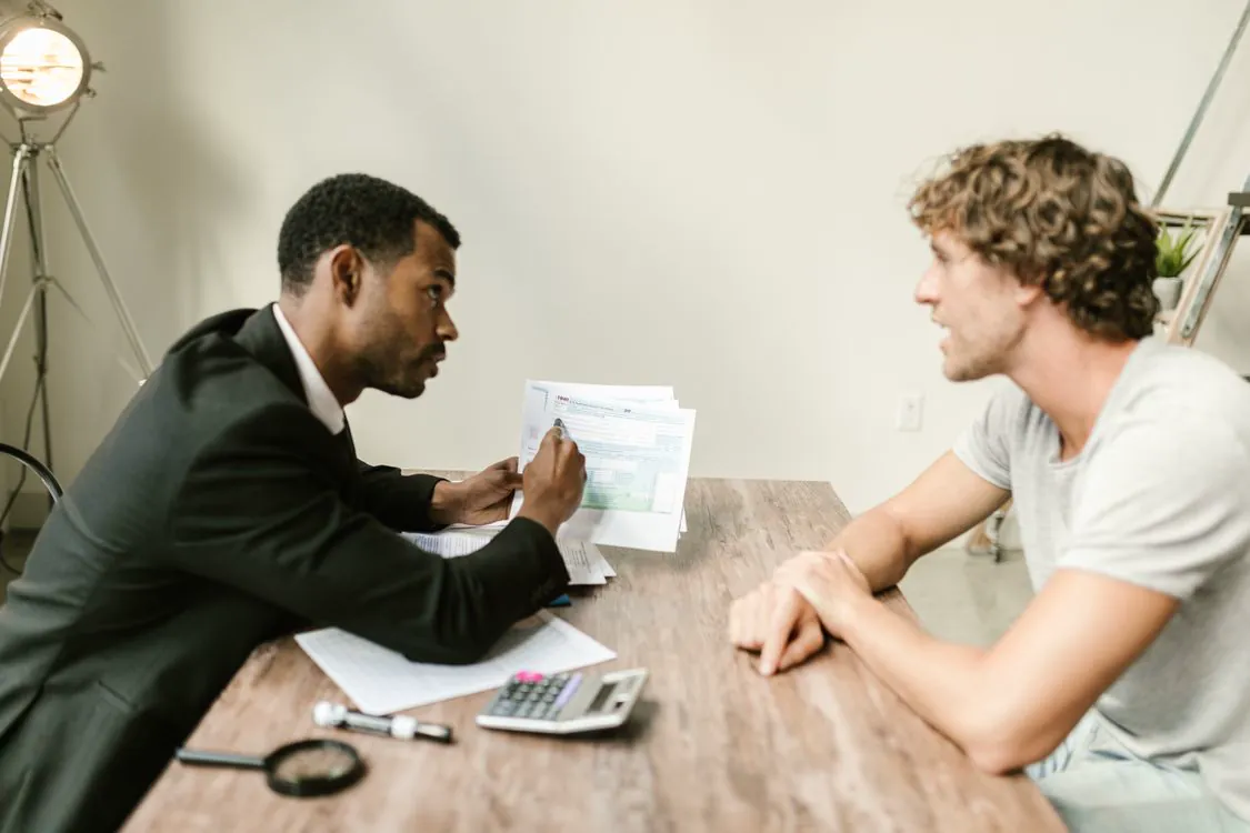 Conseiller et client échangeant autour de documents financiers et d’une calculatrice.