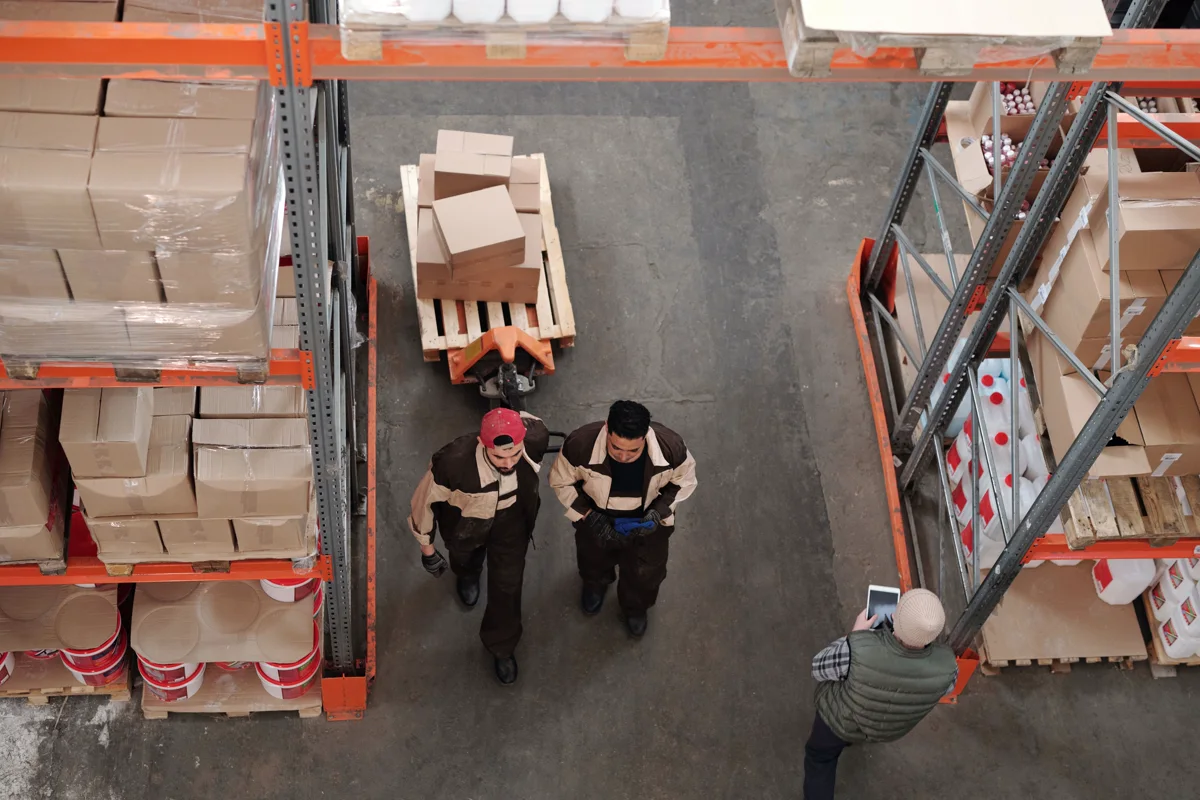 Équipe dans une allée d’entrepôt, entre les palettes, cartons et rayonnages de stockage.